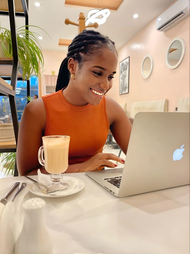 A woman smiling and scrolling on her laptop with a cup of juice beside her